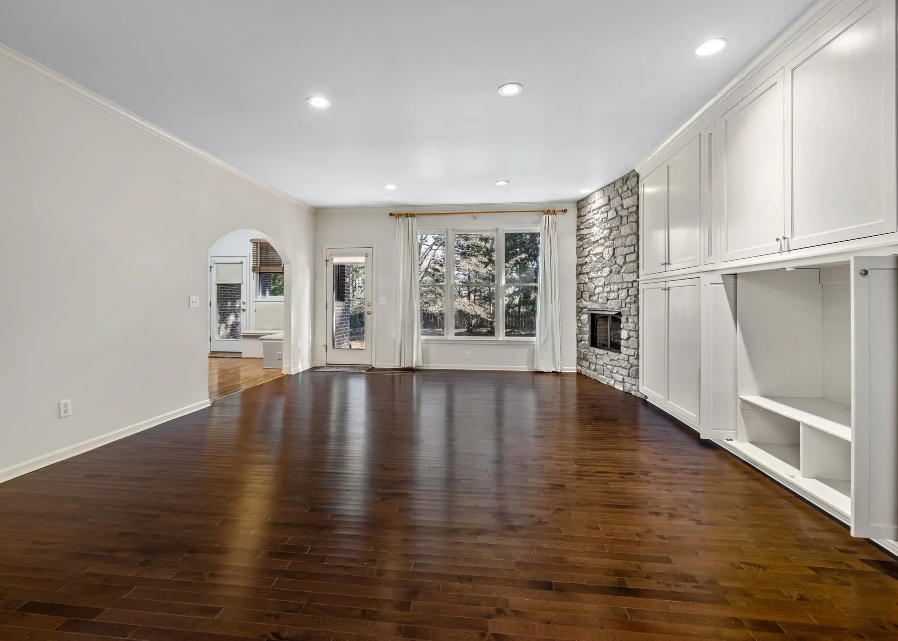 A finished living room with hardwood flooring, built-in cabinetry and a stone fireplace