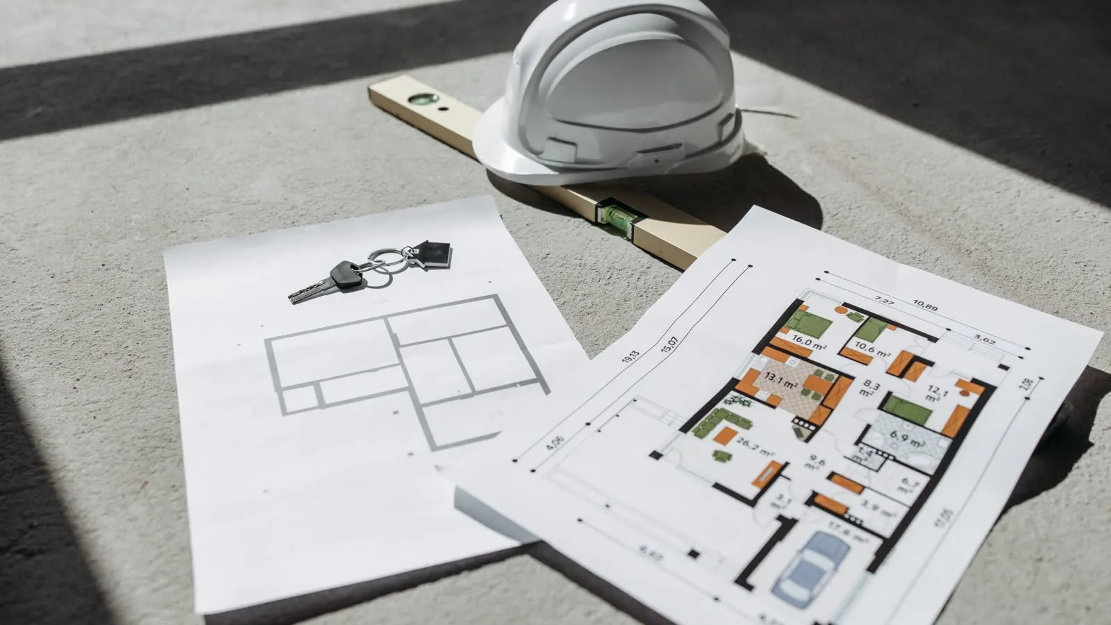 A hard hat, spirit level and floor plans laid out on a workbench
